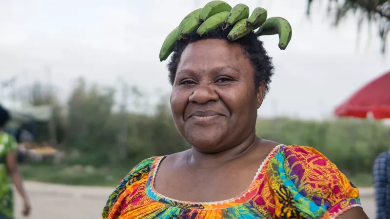 Woman carrying green bananas on top of her head in the streets of Port Moresby