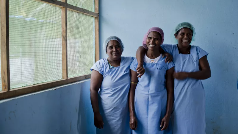 three female factory employees stand together sharing a moment of laughter