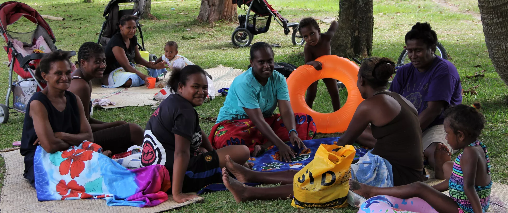 Mothers and their toddlers spending a Sunday afternoon under the palm trees next to the beach, Vanuatu.