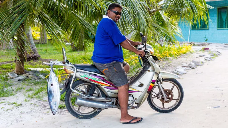 A man on a motorcycle with a tuna fish catch at Vaiaku Village in Tuvalu