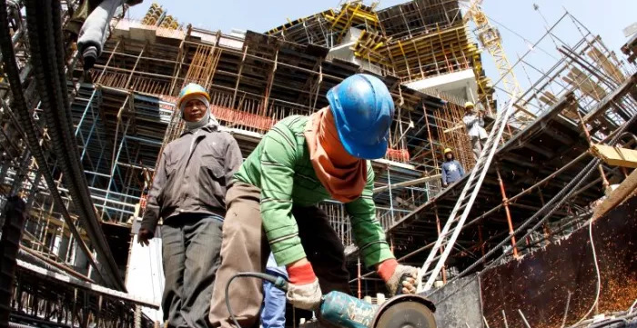 A migrant worker cuts through a metal rod at a construction site.