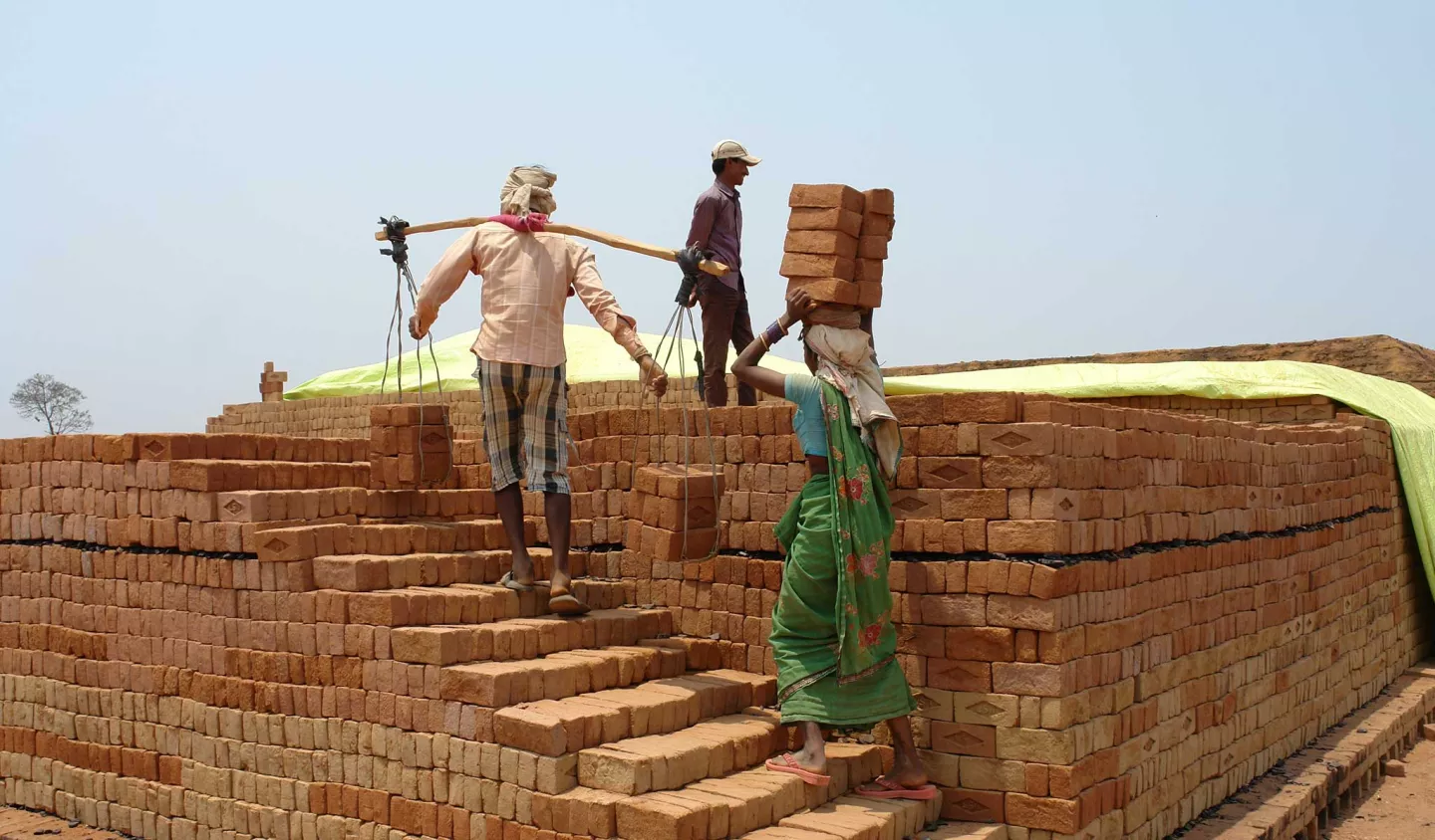 Forced labour in brick-making - A woman and a man carry heavy loads of bricks on their heads and shoulders