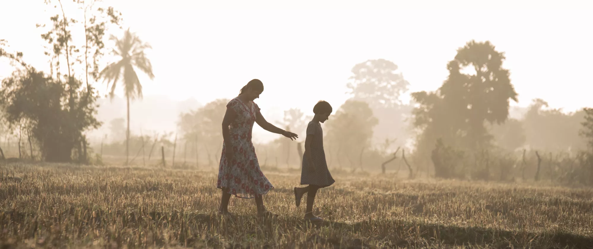 mother and young daughter walk amidst a paddy field enveloped by mist