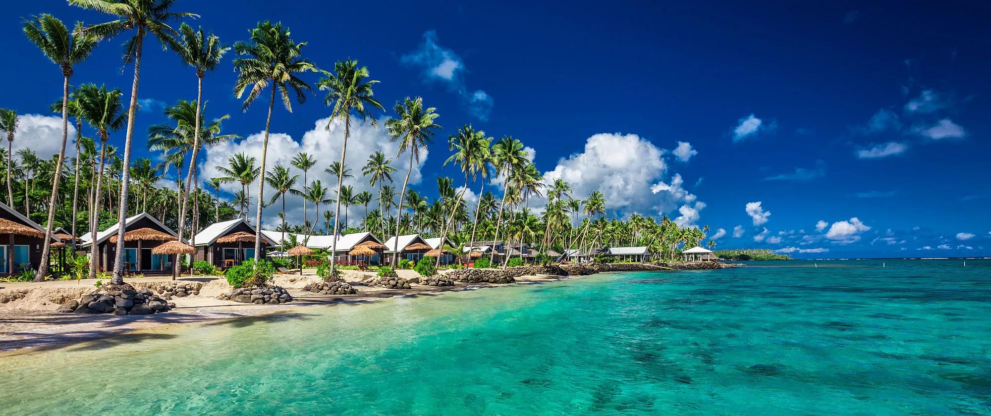 Tropical beach with coconut palm trees and villas on Samoa Island