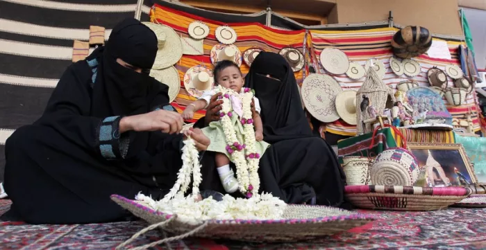 A Saudi woman threads fresh flowers together to sell in a souk