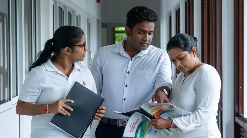 A man and 2 women walk along a corridor while examining a training manual book 