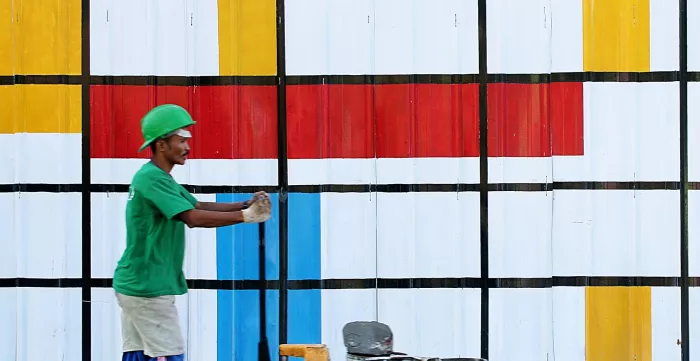 Man pushing a cart with paint buckets in front of a colourful wall.