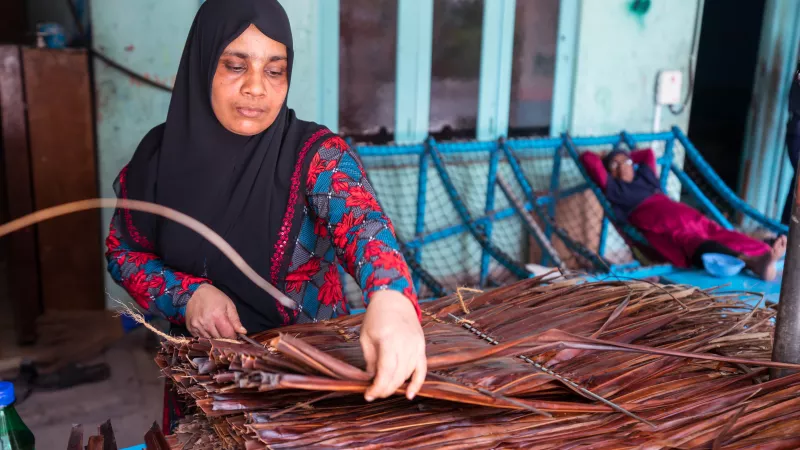 A woman weaves using palm leaves