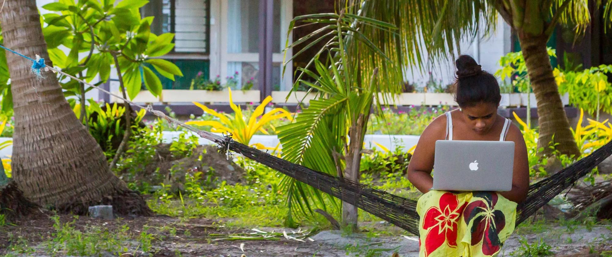 A woman with a notebook working outdoors under palm trees in Tuvalu