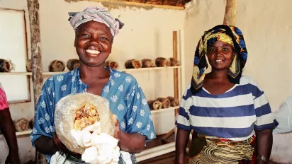 Two Tanzanian women smile at the camera, one holding a bag of mushroom