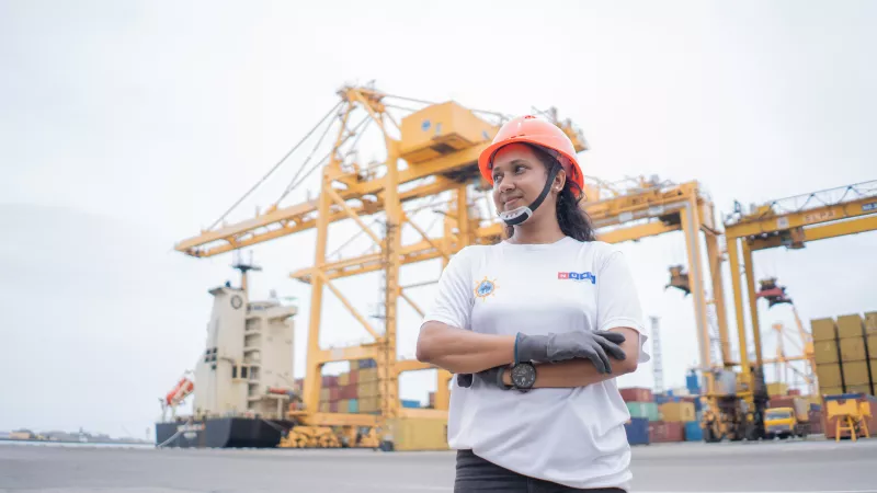 woman transfer crane operator stands with arms crossed in bustling Colombo port