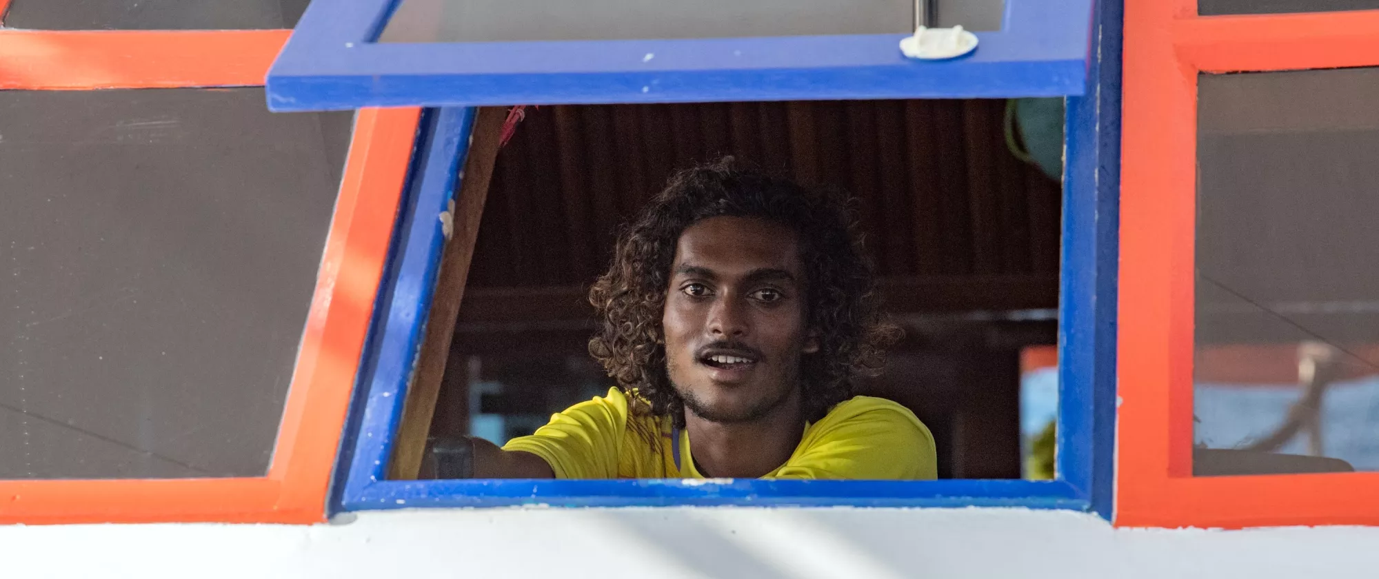 A young man smiles at the camera from inside a boat